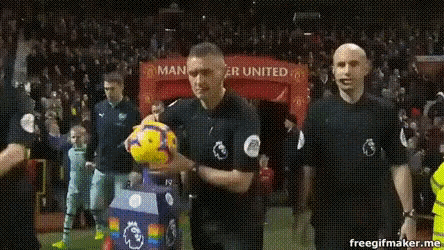 a referee holding a soccer ball in front of a sign that says manchester united