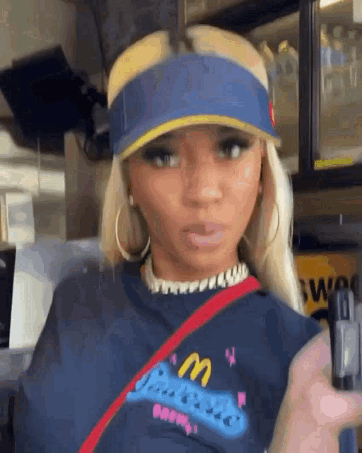 a woman wearing a blue visor and a mcdonald 's shirt is standing in a restaurant .