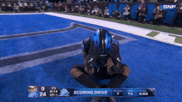 a football player kneeling on the field with a scoreboard displaying the scoring drive