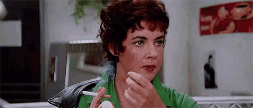 a woman is smoking a cigarette in a kitchen while eating a sandwich .