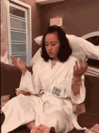 a woman in a bathrobe is sitting on a couch holding a bunch of money .
