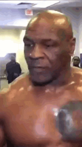 a man without a shirt is holding a boxing glove in his hand and looking at the camera .