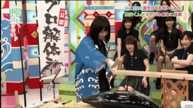 a woman in a blue robe is cutting a large fish in front of a group of girls