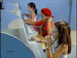 a boy in a red hat sits on a girl 's lap using a computer