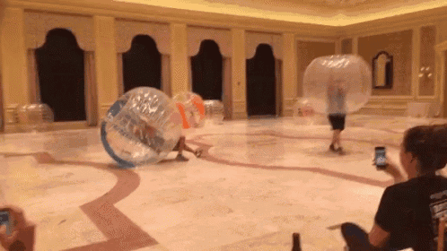 a group of people are playing with bubble balls in a large hallway .