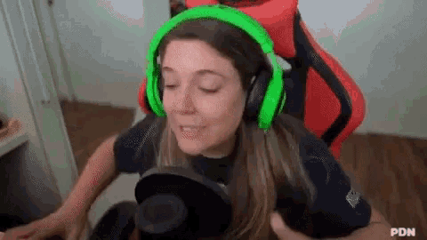 a woman wearing green headphones is sitting in a red gaming chair .