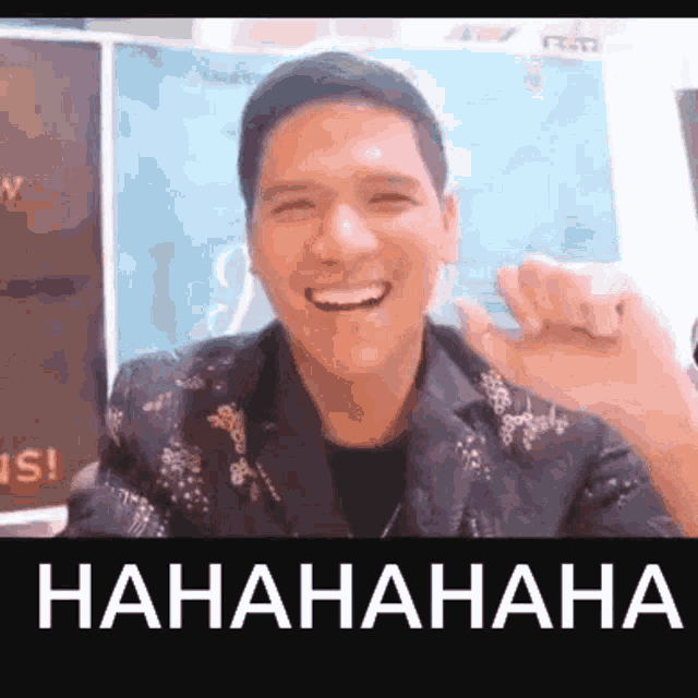 a man in a suit is smiling and making a funny face in front of a sign that says ' hahahahaha '