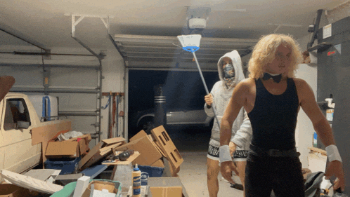 a man in a bow tie is holding a mop in a garage next to a woman in a hoodie