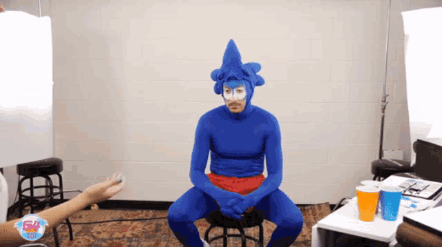 a man in a sonic costume sits on a stool in front of a white wall