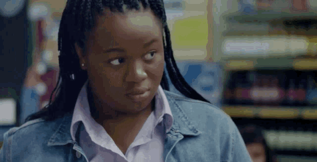 a woman with braids is wearing a denim jacket and a white shirt .