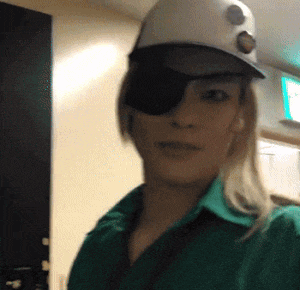a woman wearing an eye patch and a hat looks at the camera
