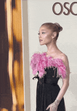a woman in a black dress with pink feathers is standing in front of a wall that says osc