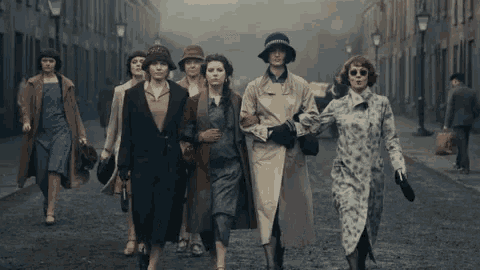 a group of women and men are walking down a street .