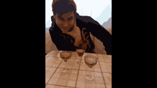 a young man sits at a table with three wine glasses on it