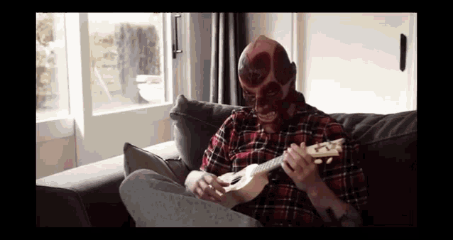 a man with a mask on his face is sitting on a couch playing a guitar