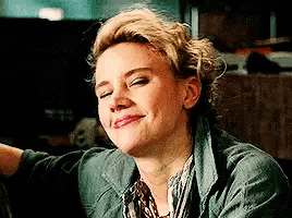 a woman with blonde hair is smiling with her eyes closed and wearing a green jacket .