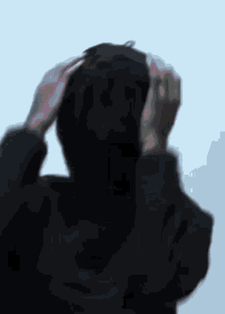 a person in a black hoodie is holding their head in their hands .