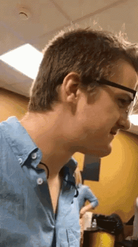 a man wearing glasses and a blue shirt looks at something