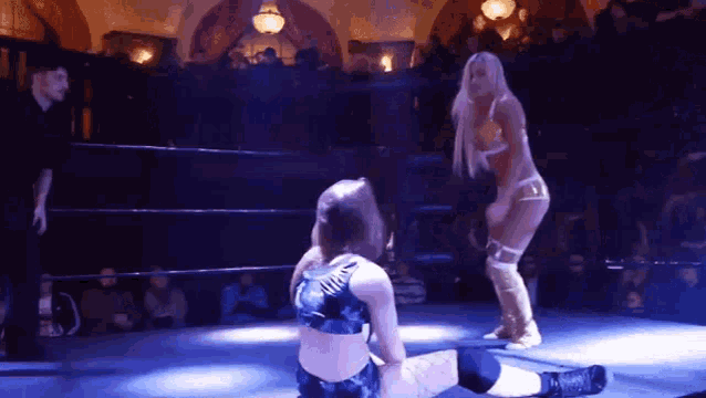 two women are wrestling in a ring while a referee looks on .