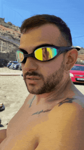 a man without a shirt is wearing sunglasses with a reflection of a red car