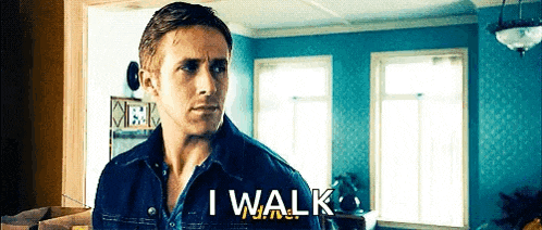 a man in a denim jacket is standing in a living room with the words i walk behind him .