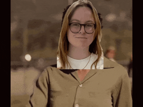 a woman wearing glasses and a tan shirt is standing in front of a dark background