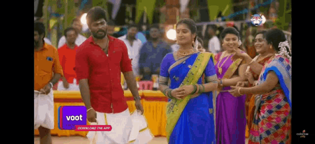 a man in a red shirt and a woman in a blue saree are dancing in front of a crowd of people .