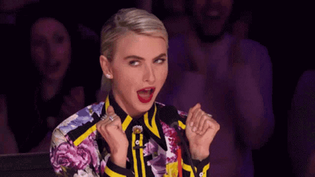 a woman in a colorful shirt is sitting in front of a crowd and making a funny face .