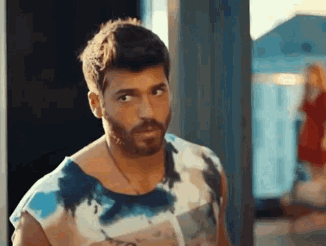 a man with a beard is wearing a tie dye t-shirt and looking at the camera .