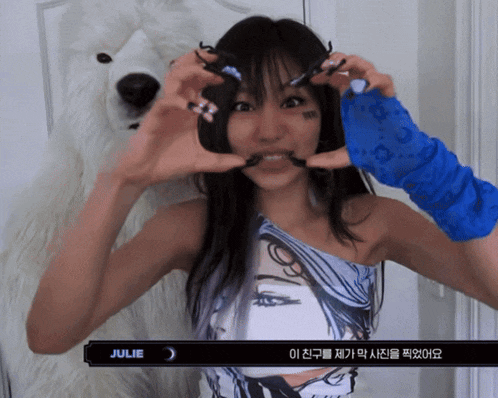 a woman making a heart with her hands in front of a white teddy bear with julie written on the bottom