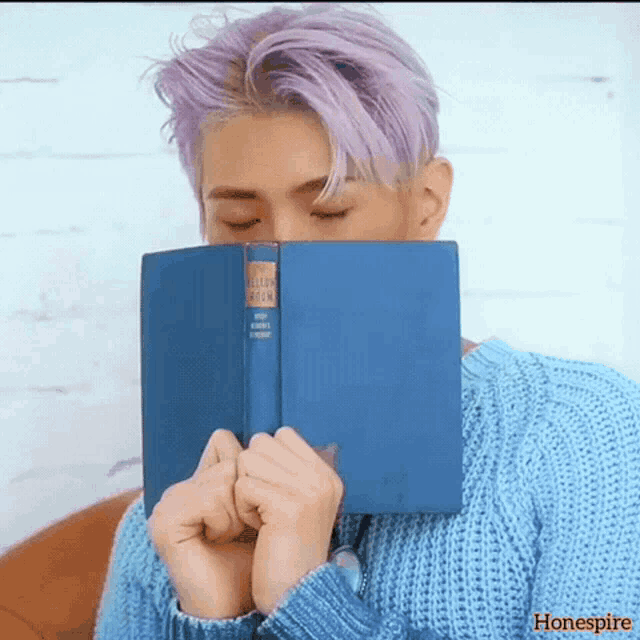 a man with purple hair is covering his face with a blue book called a killer book