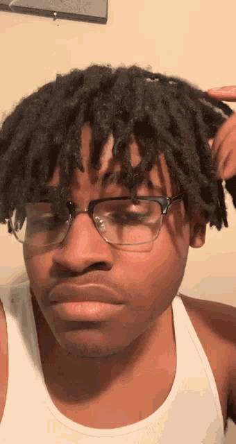 a young man wearing glasses and a white tank top looks at the camera