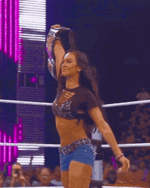 a woman in a crop top and shorts is standing in a ring with her arms outstretched .
