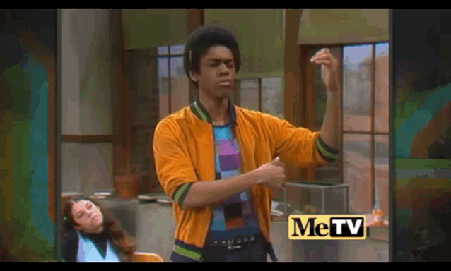 a man in a yellow jacket is standing in front of a window with the word metv on the bottom right