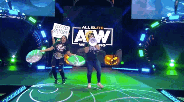 a couple of women holding signs in front of a sign that says all elite wrestling