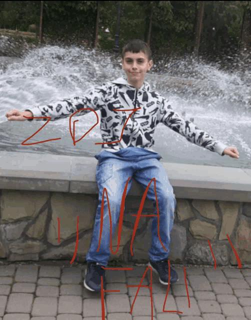 a boy sitting on a stone wall with a fountain in the background and the word zona written in red