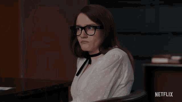 a woman with glasses and a choker sits in front of a netflix sign