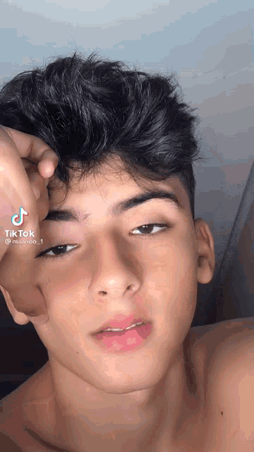 a young man without a shirt is taking a selfie with his hand on his forehead .