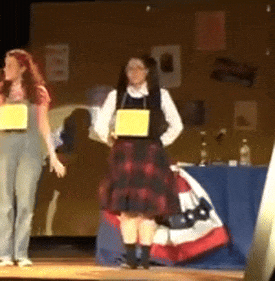 a woman in a plaid skirt is holding a yellow sign that says ' i 'm a ' on it
