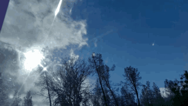 a blue sky with trees in the foreground and clouds in the background