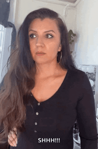 a woman with long hair is wearing a black shirt and making a funny face .
