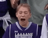 a young boy in a purple basketball jersey is screaming while sitting in the stands .