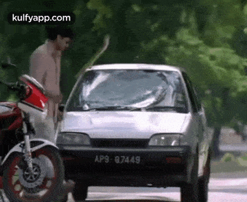 a man is standing next to a motorcycle and a car with a broken windshield .