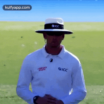 a man wearing a hat and sunglasses is standing in front of a field .
