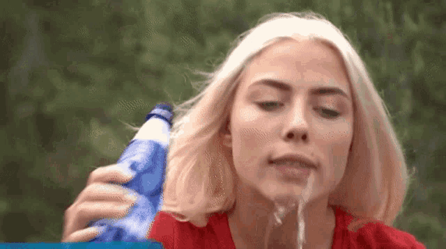 a woman in a red shirt is pouring water from a blue bottle into her mouth .