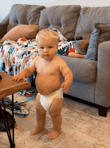 a baby in a diaper is walking in front of a couch