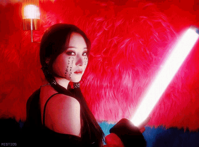 a woman holding a light in front of a red furry wall with mistios written below her