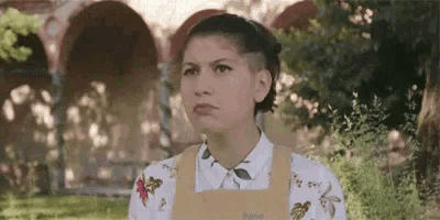 a woman wearing a yellow apron and a white shirt is standing in a park .