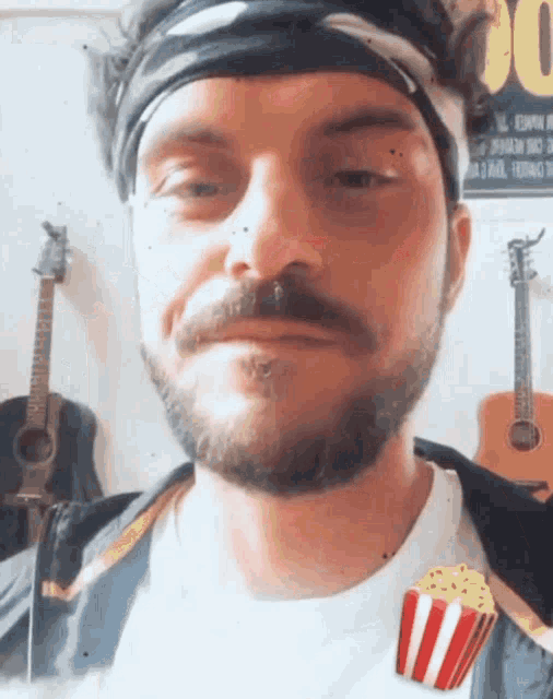 a man with a beard and a bandana on his head is holding a popcorn box
