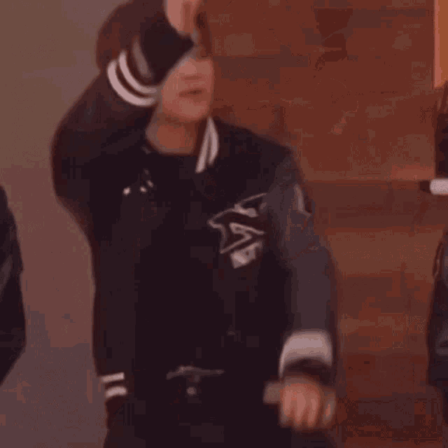 a man in a baseball jacket is dancing in a room with his hands in the air .